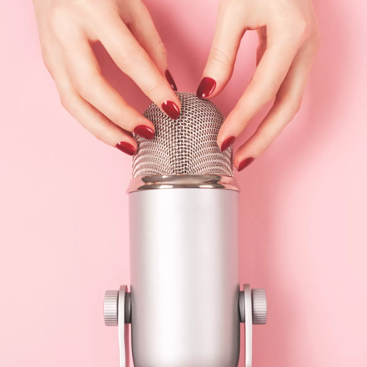Hands tapping a microphone against a soft pink background